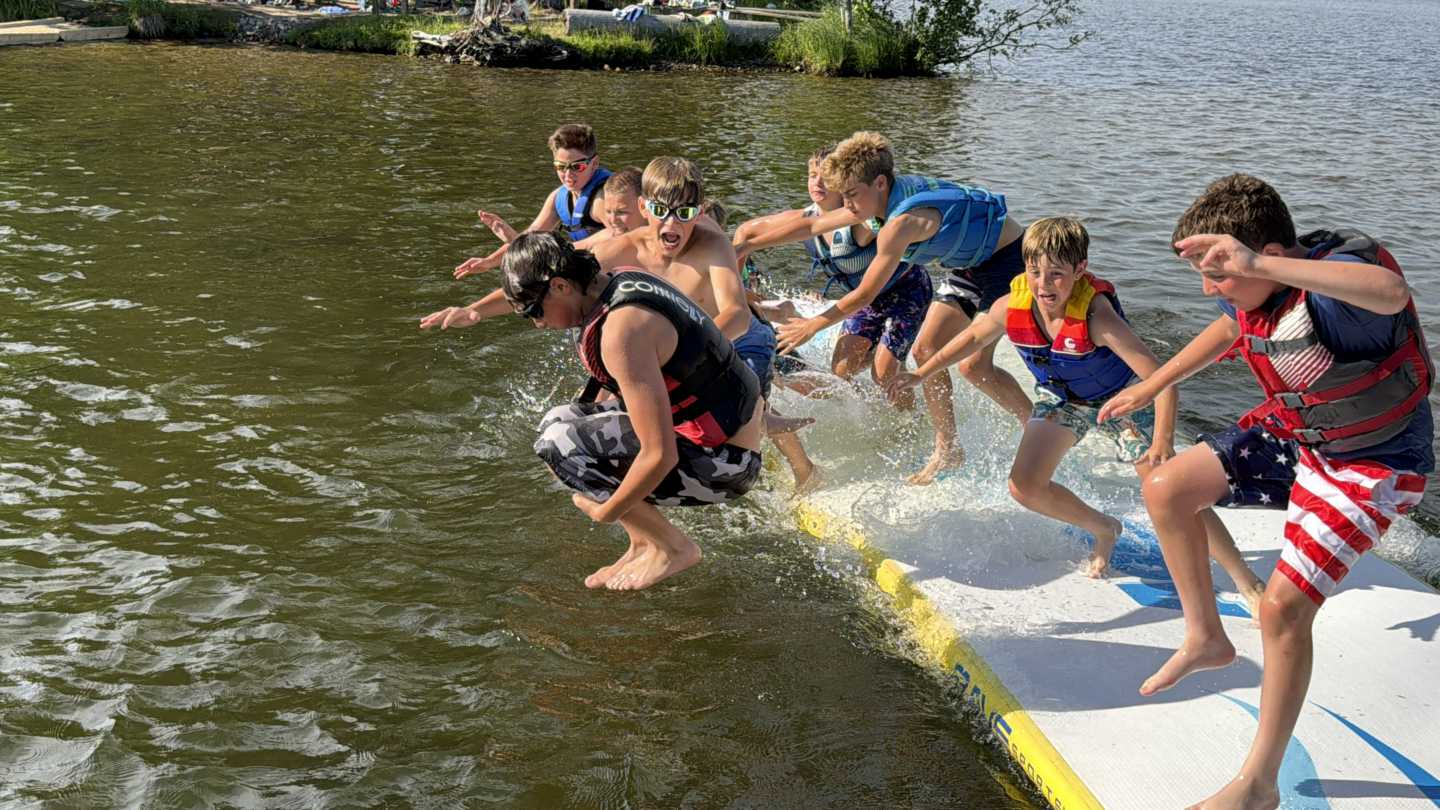 Campers leap off floating splash mats into the lake during free swim